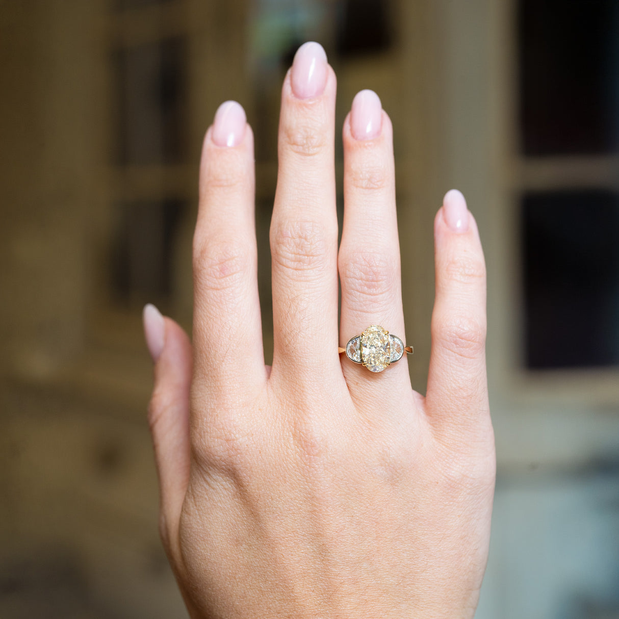 Vintage yellow oval diamond and half-moon diamond three-stone ring worn on hand with elongated centre diamond.