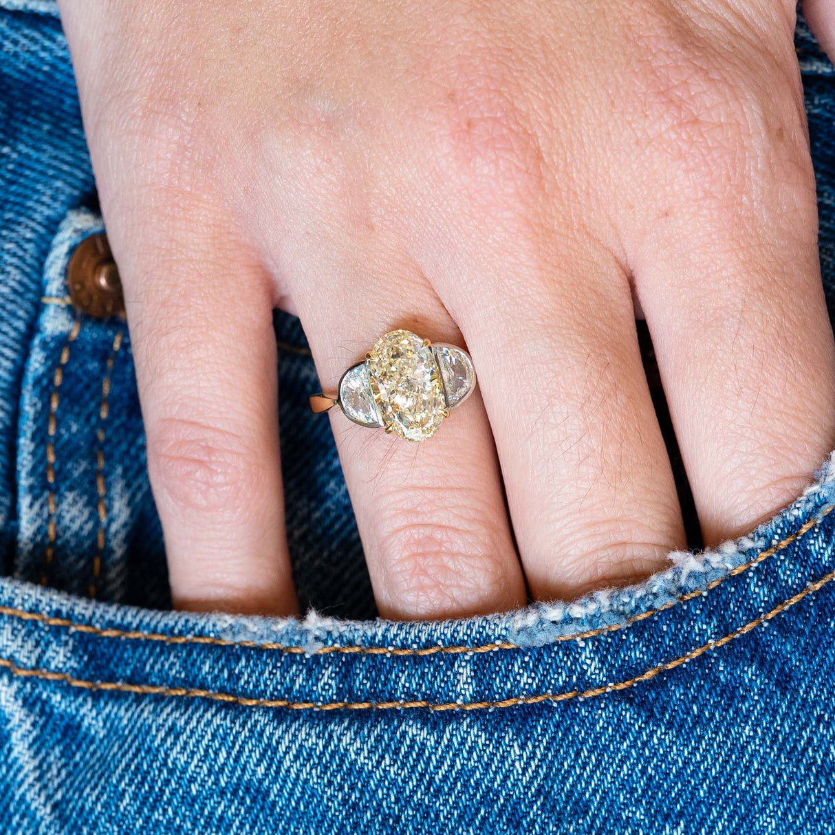 Vintage yellow oval diamond and half-moon diamond three-stone ring worn on hand resting in denim pocket.