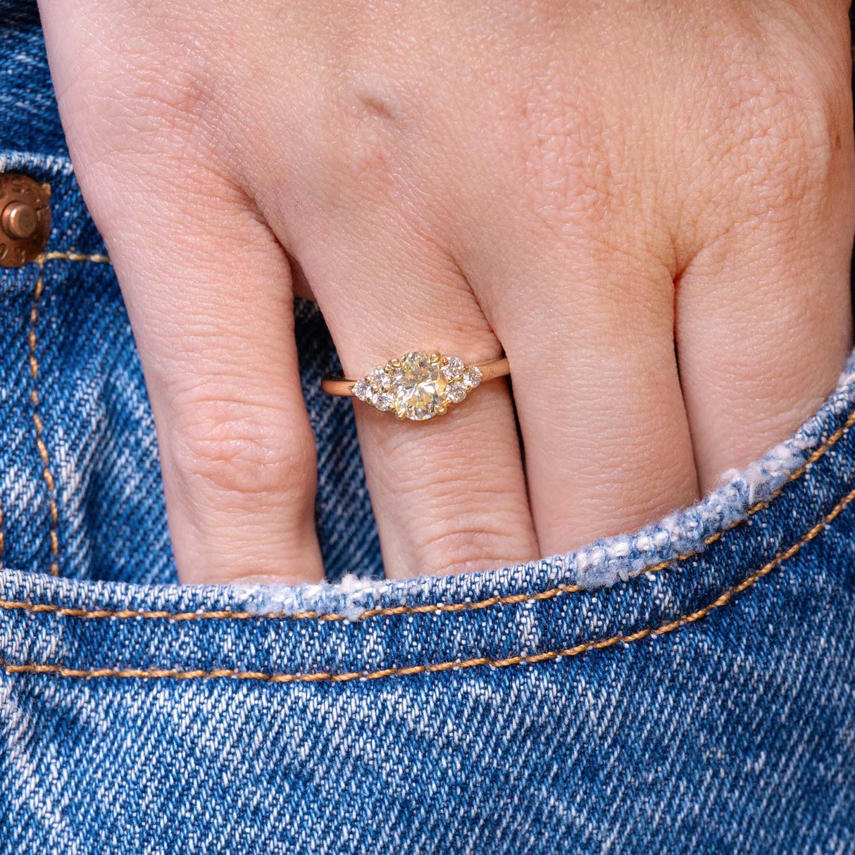 Antique-inspired primrose yellow diamond cluster tre-foil engagement ring worn on hand with denim pocket styling.