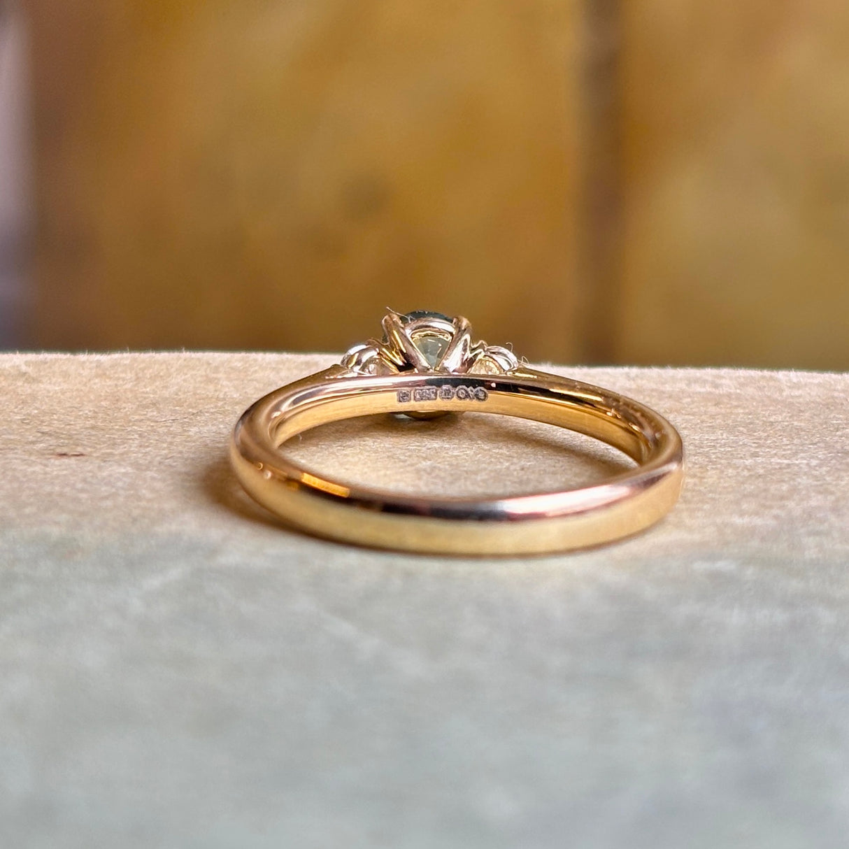 Rear view of yellow gold three-stone ring with teal sapphire centre and diamond accents.