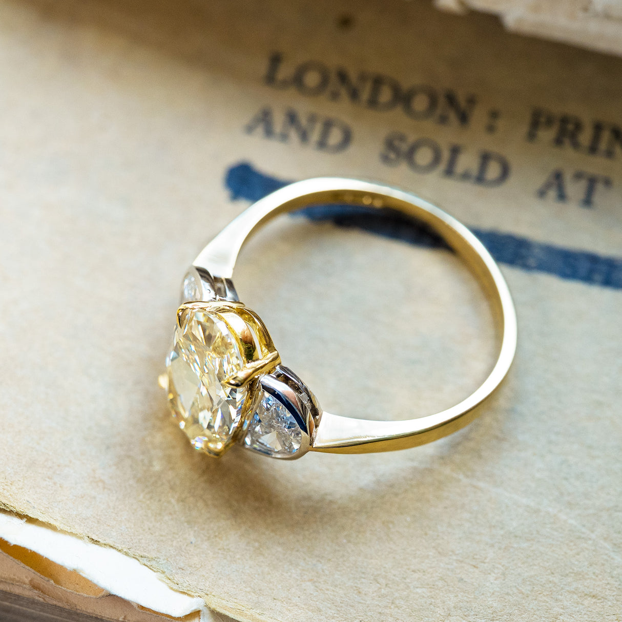 Vintage yellow oval diamond three-stone ring with half-moon side diamonds and polished gold band.