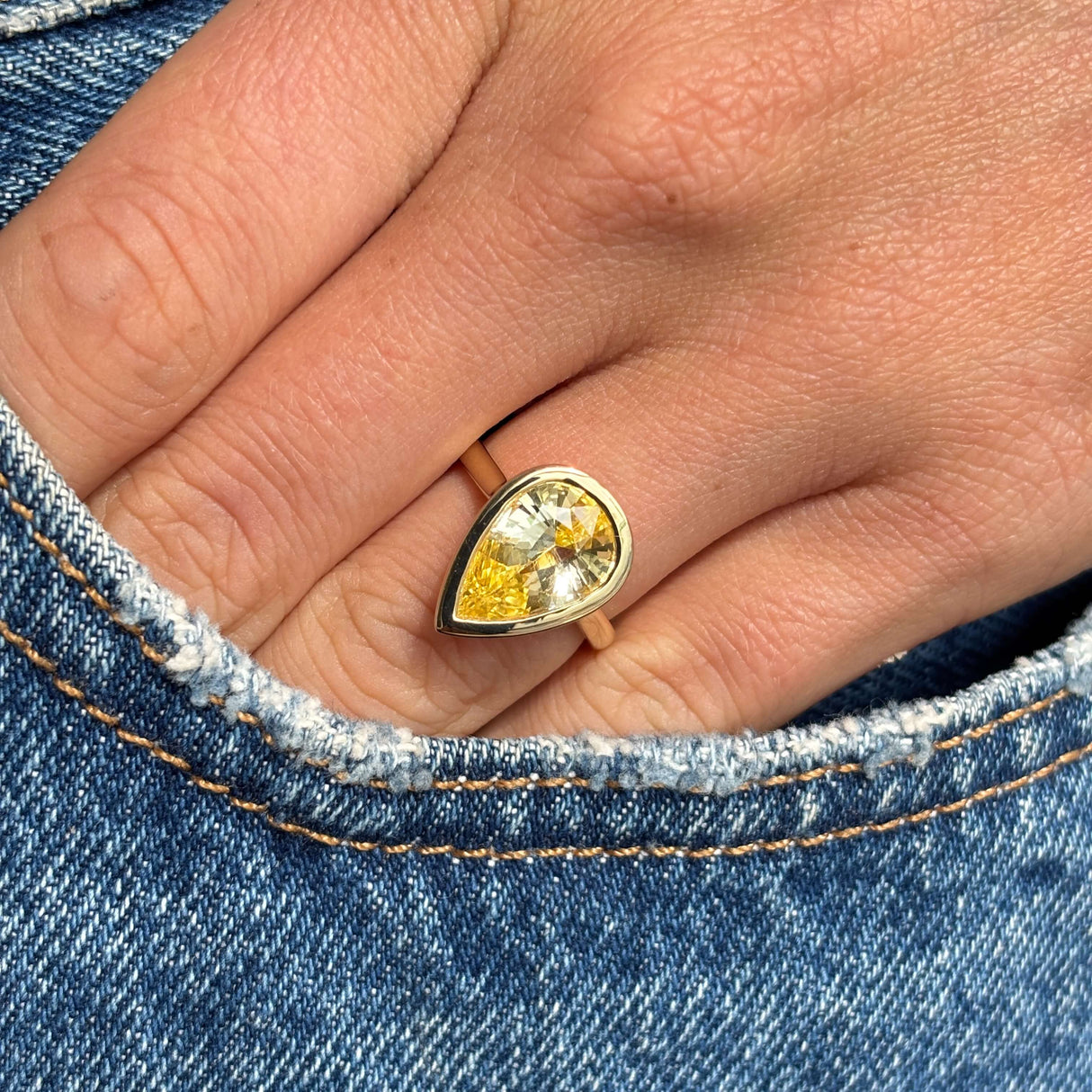 Antique-inspired yellow gold solitaire ring with a large pear-cut Sri Lankan yellow sapphire, styled on hand against blue denim to highlight the gemstone's vivid colour and elegant proportions.