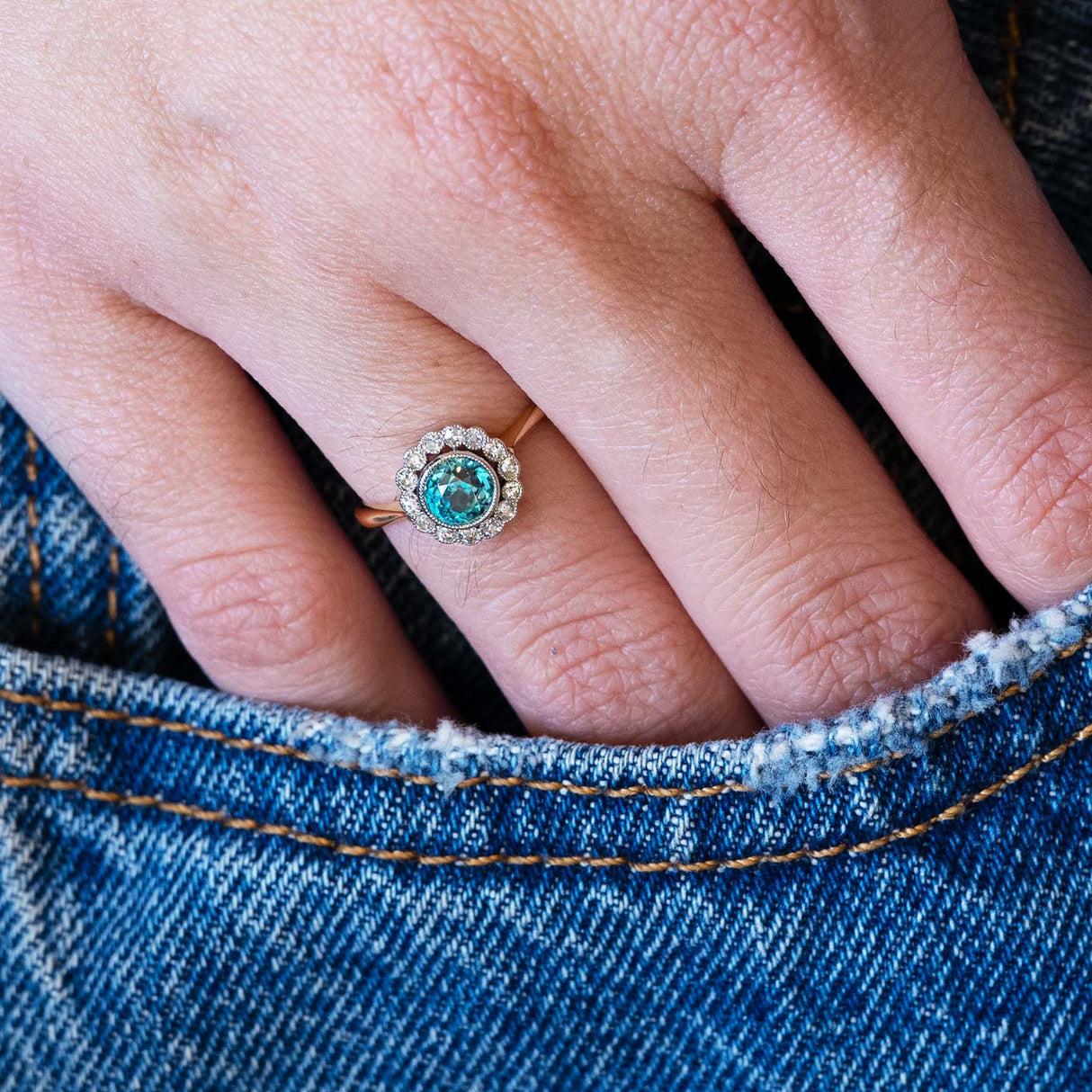 Close-up of a hand wearing an antique zircon ring with a denim pocket detail.