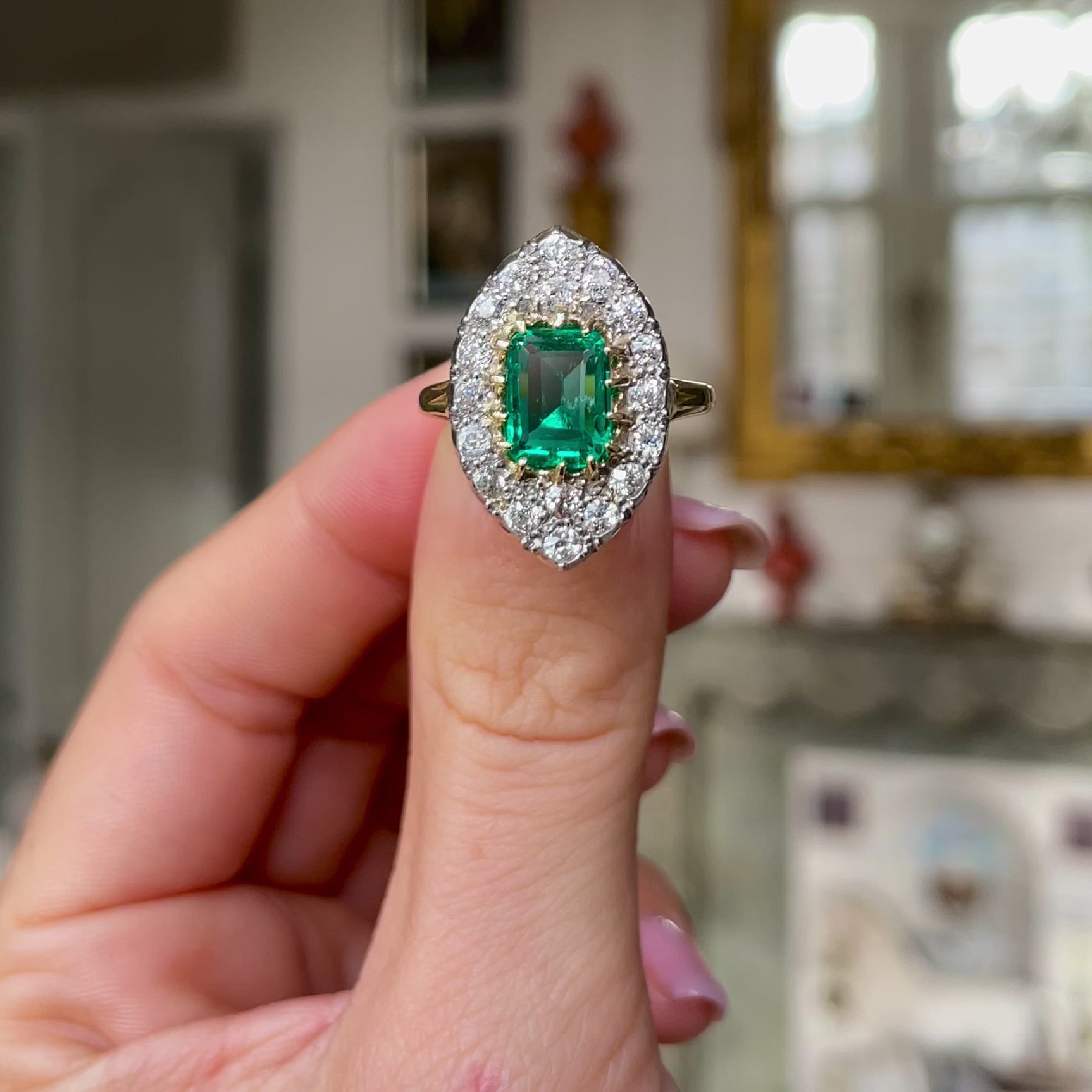 Emerald and diamond navette ring, held in fingers and rotated to give perspective.