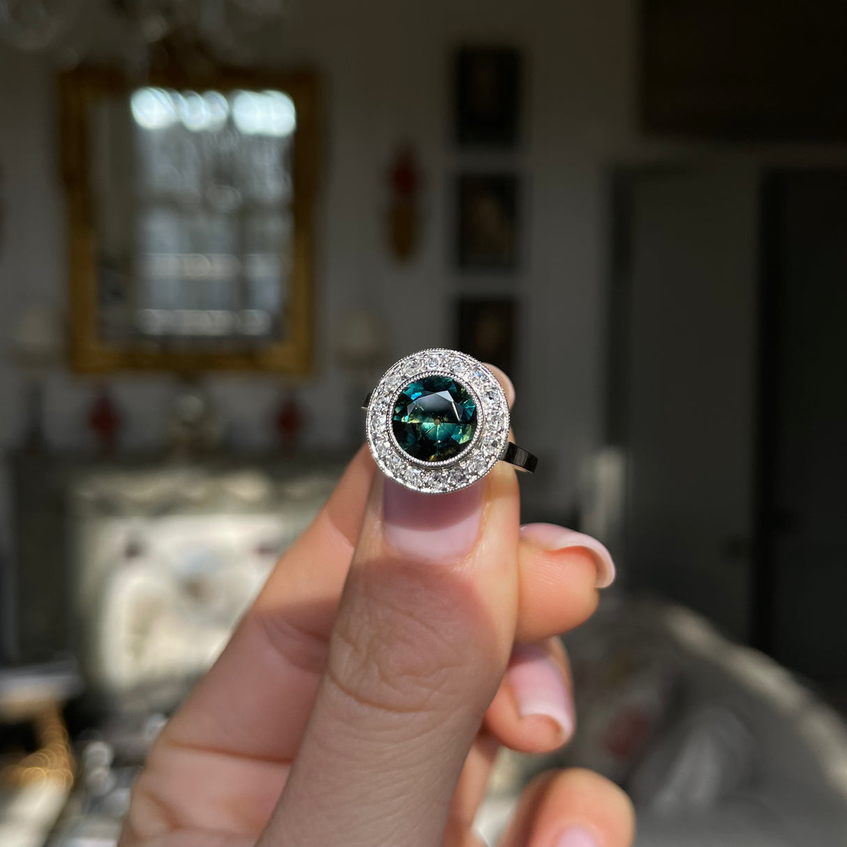 green yellow sapphire and diamond cluster ring, held in fingers.