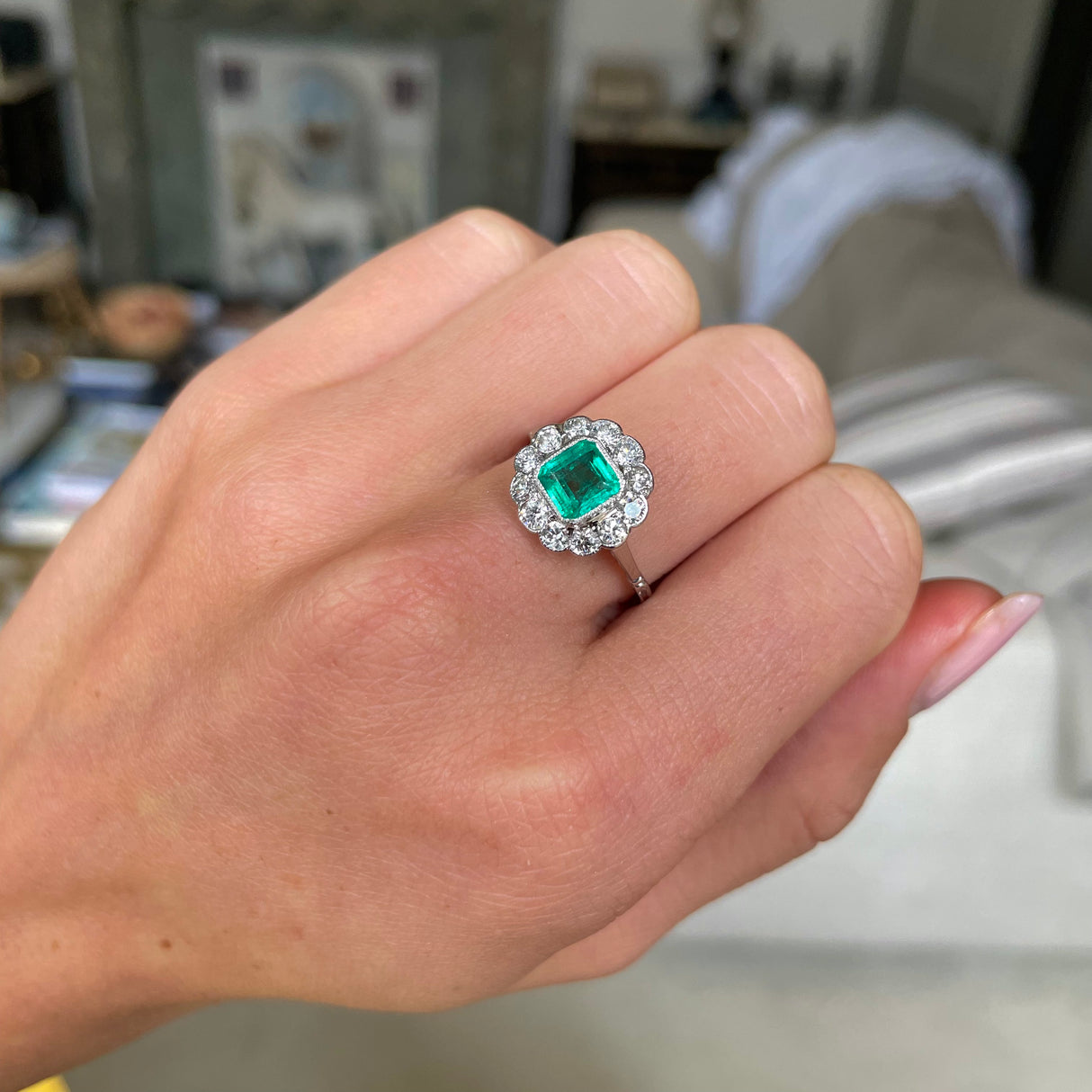 Edwardian emerald and diamond cluster ring, worn on hand.