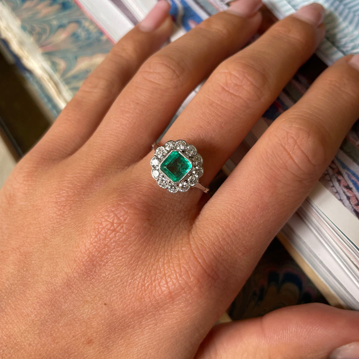 Edwardian emerald and diamond cluster ring, worn on hand.