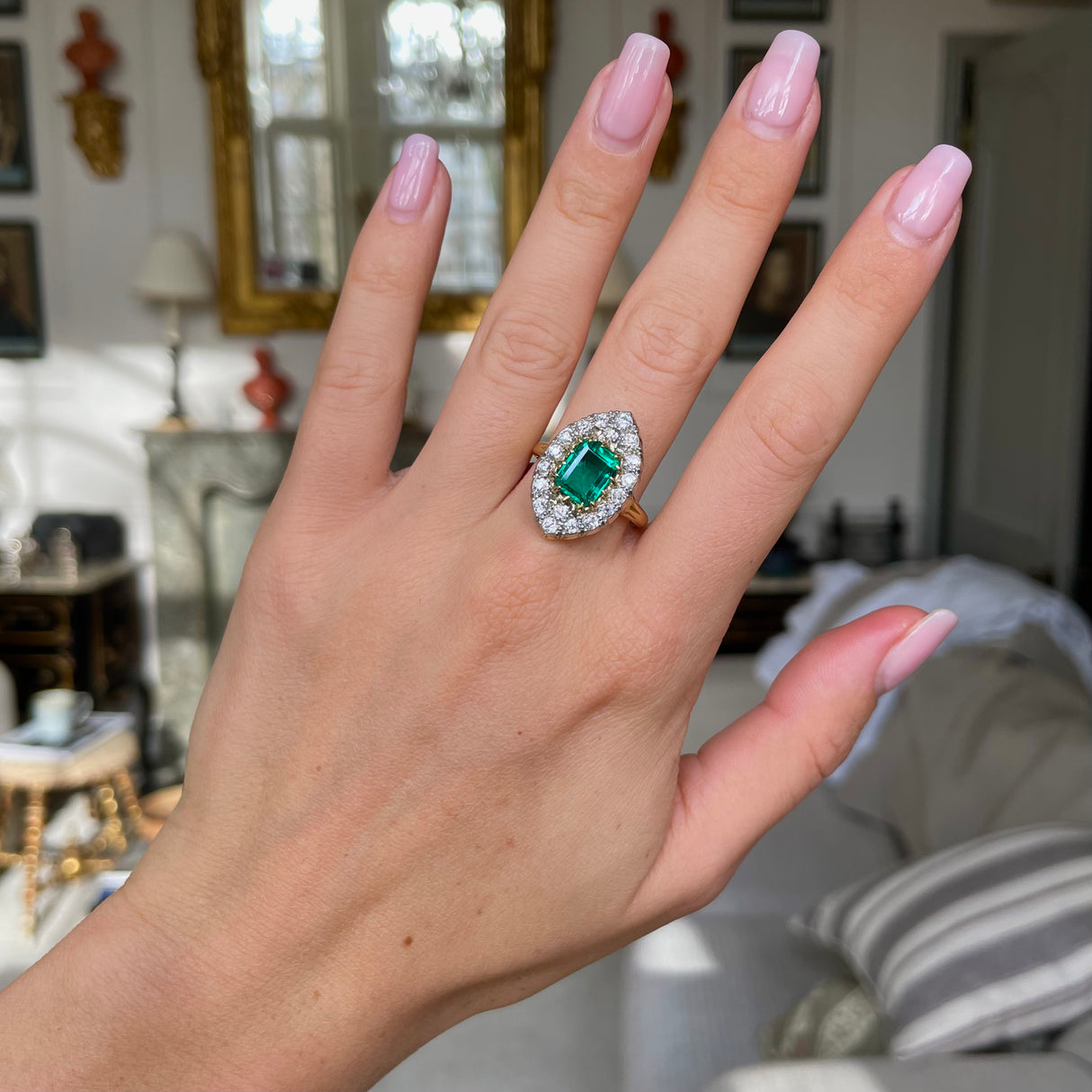 Emerald and diamond navette ring, worn on hand.