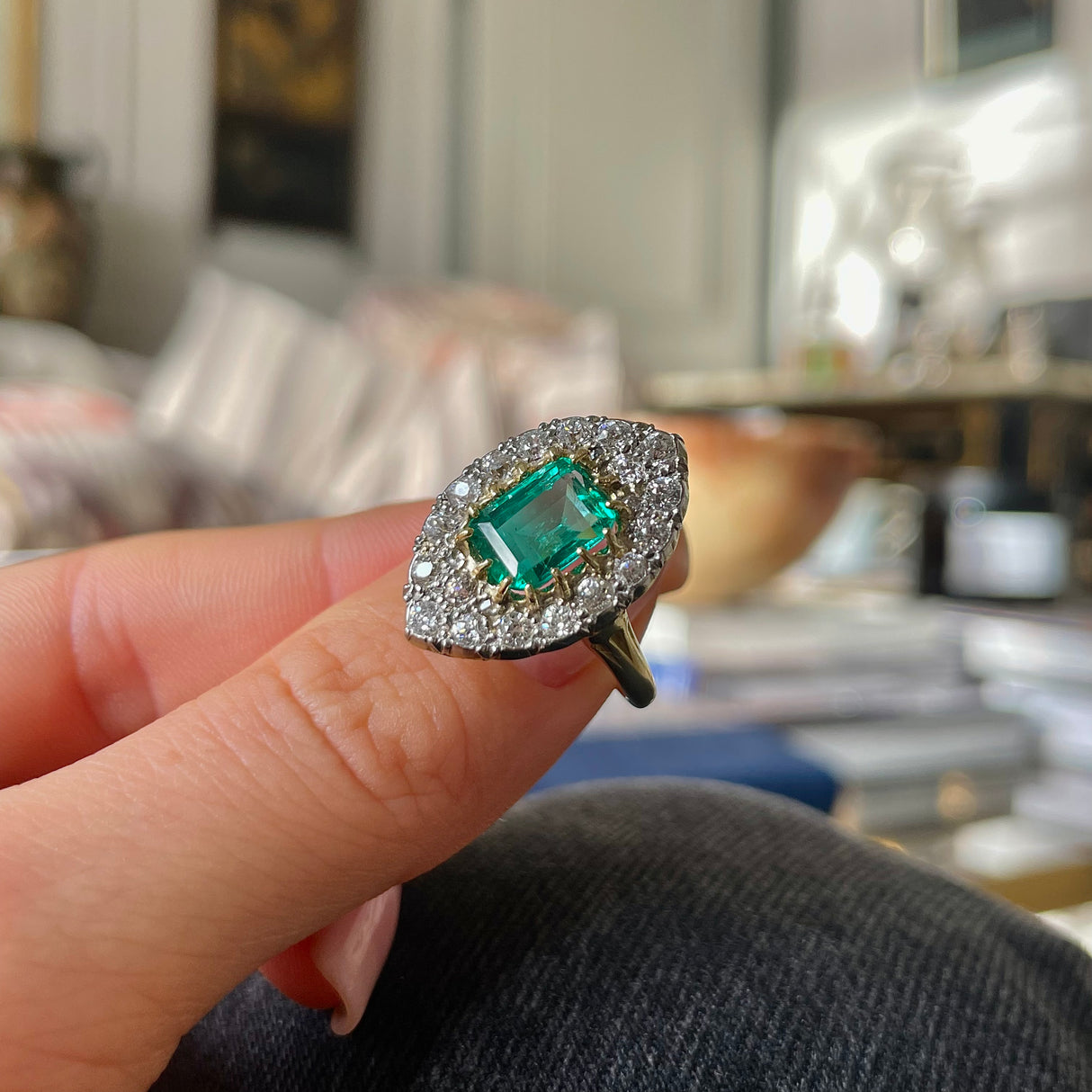 Emerald and diamond navette ring, held in fingers.