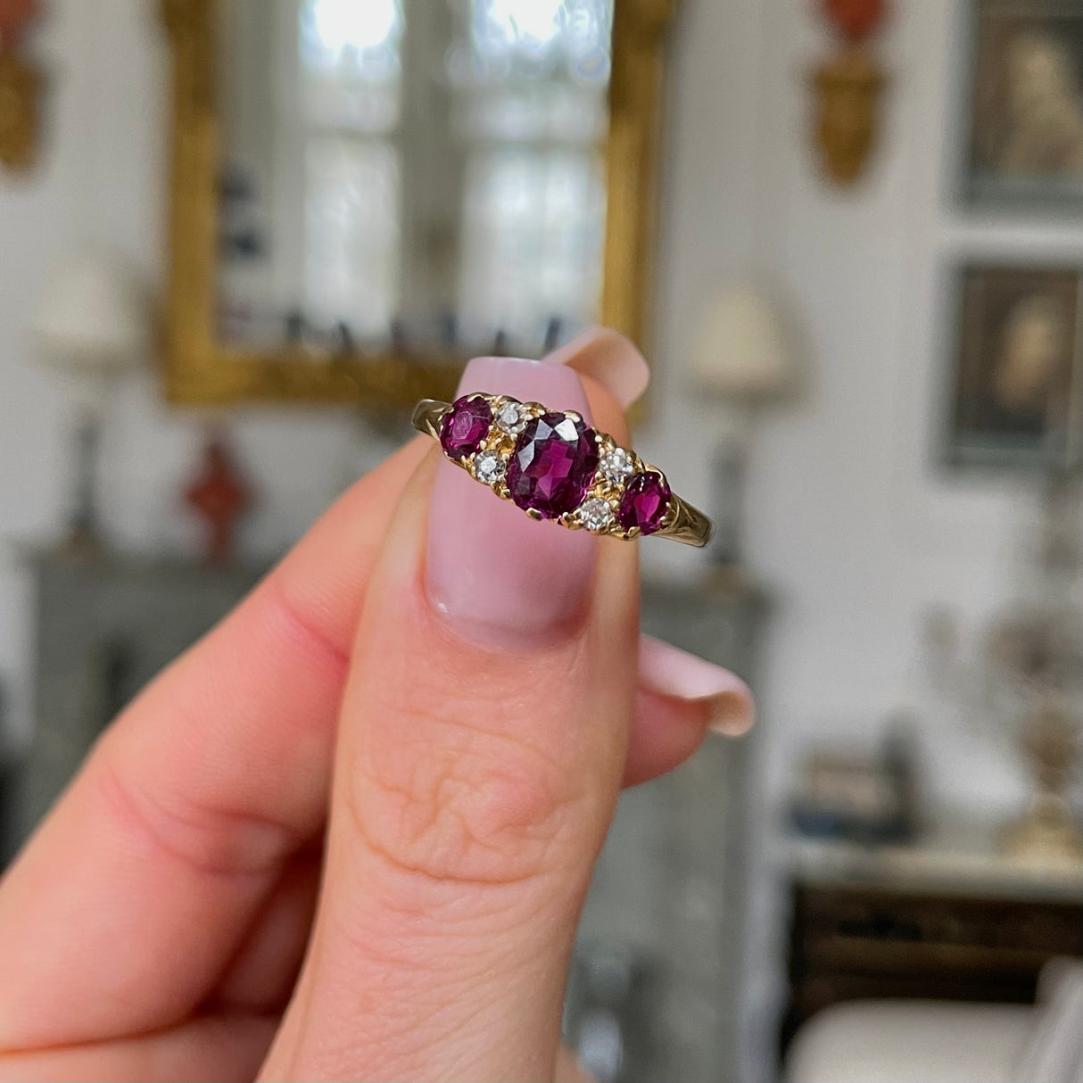 Antique Edwardian three stone ruby and diamond ring, held in fingers.