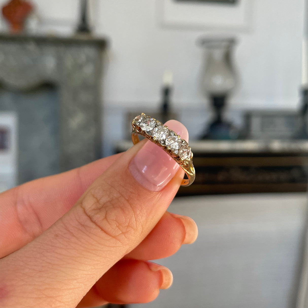 Antique five-stone diamond engagement ring, held in fingers.