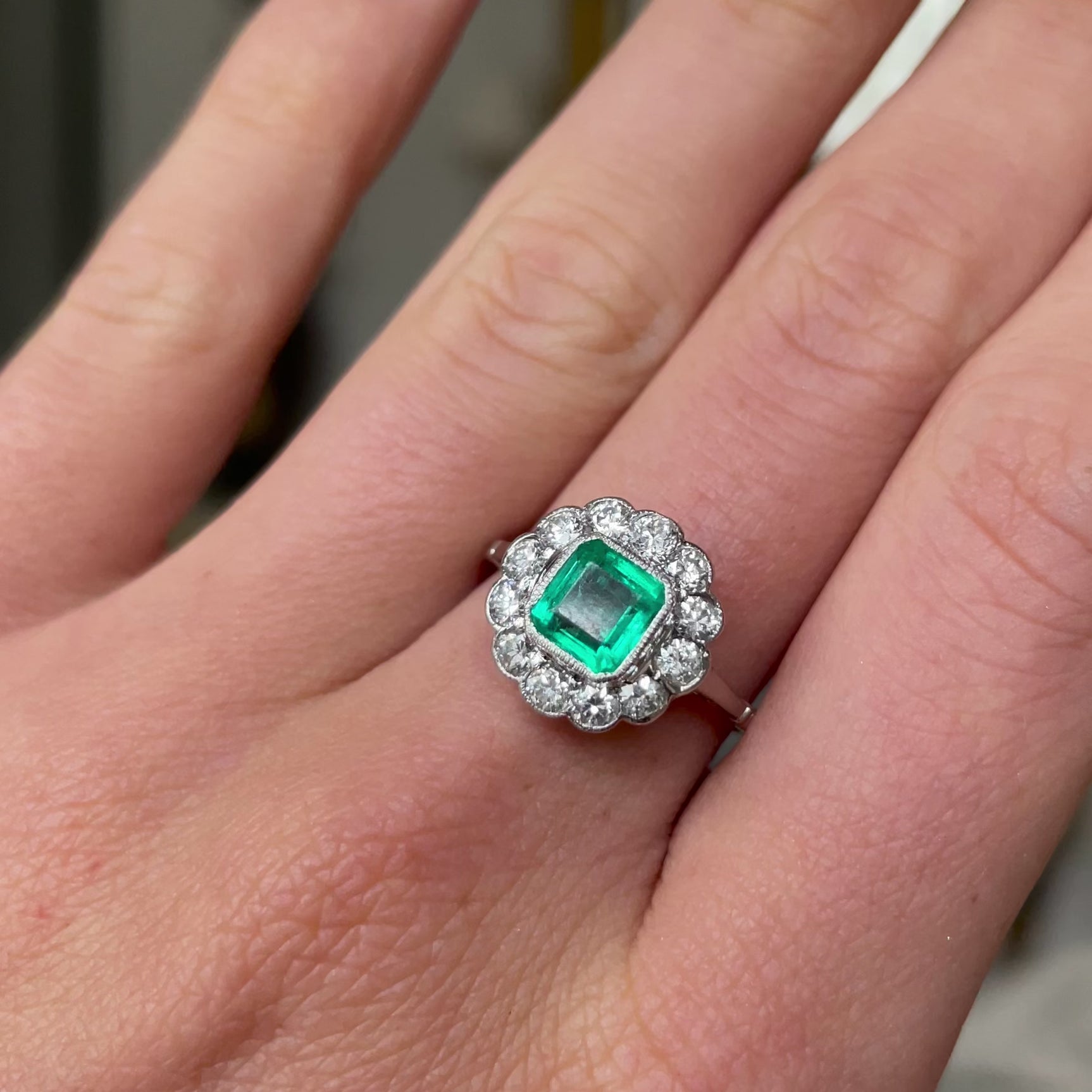 Edwardian emerald and diamond cluster ring, worn on hand and rotated to give perspective.