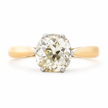 A front profile of an antique, Edwardian yellow tinted cushion-shaped old-cut diamond solitaire engagement ring with a yellow gold band.