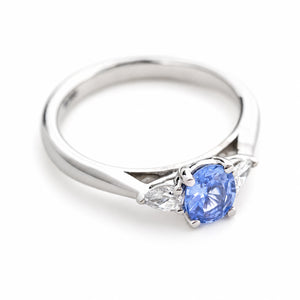 A vintage-inspired platinum engagement ring with a pale blue-purple sapphire centre stone flanked by pear-cut diamonds. 