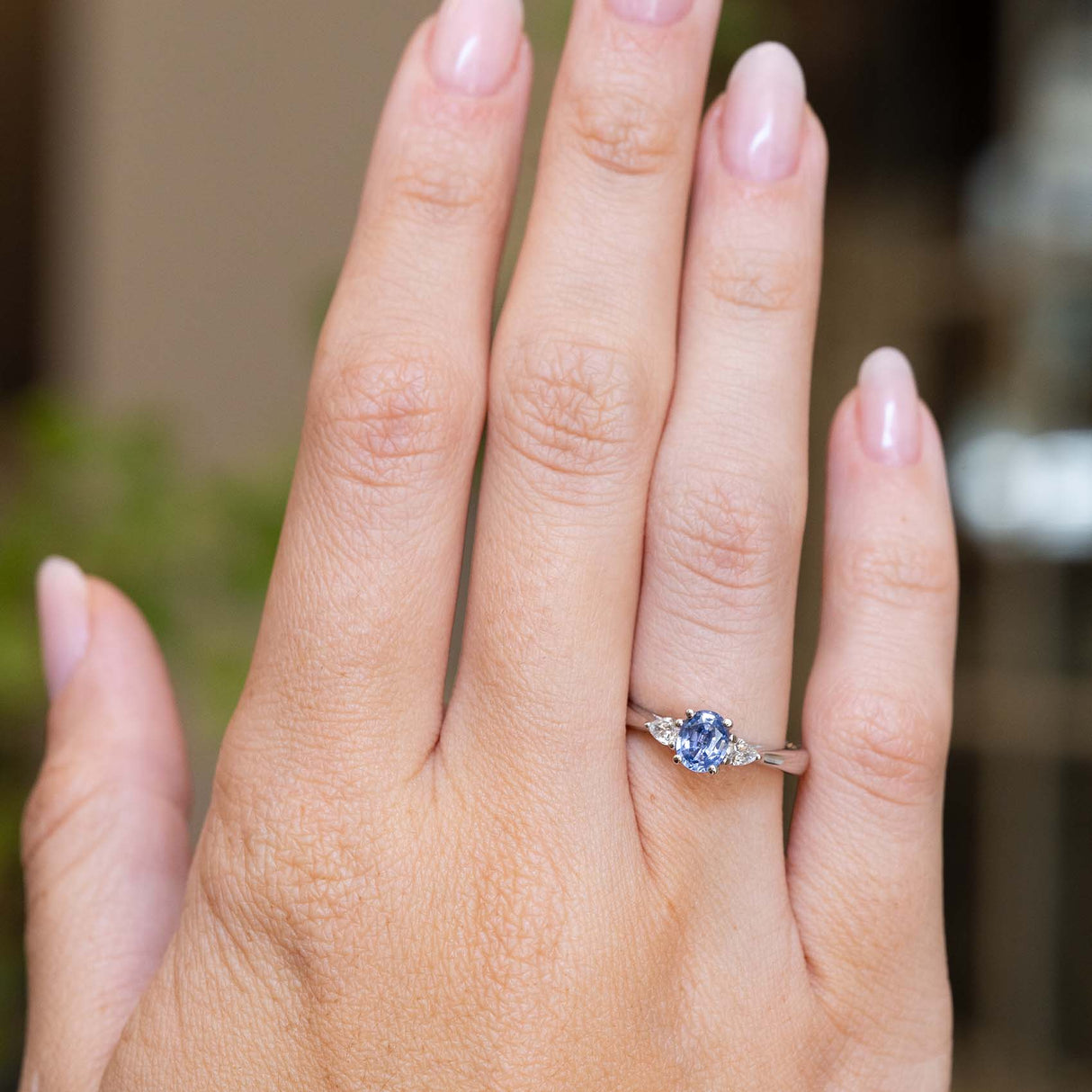 A vintage-inspired light blue sapphire and diamond three-stone engagement ring worn on the hand.