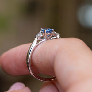 Gallery detail of a vintage-inspired light blue sapphire and diamond three-stone engagement ring held between the fingers.