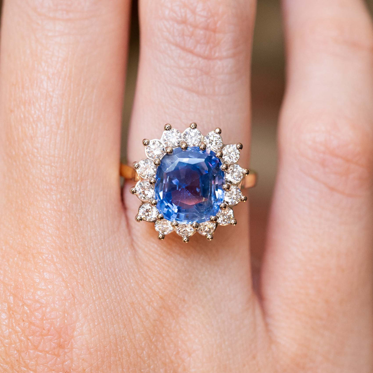 An antique-inspired Ceylon blue sapphire and diamond cluster engagement ring in yellow and white gold, worn on a hand.