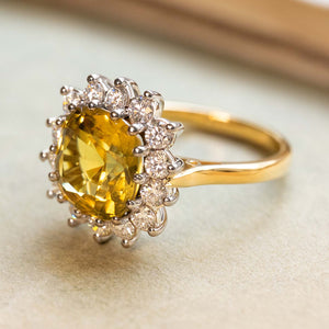 A three-quarter profile of an antique-inspired, yellow sapphire and diamond cluster displayed on a book.