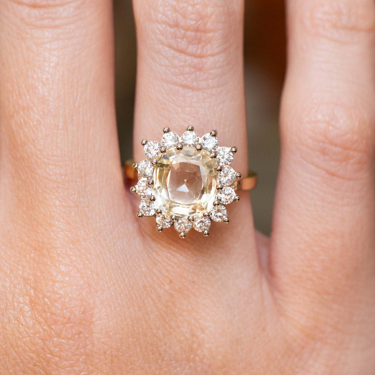 A close-up of a ring worn on a finger, featuring an antique-inspired, yellow Ceylon sapphire and diamond halo in yellow gold.