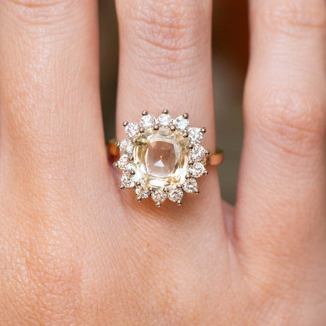 A close-up of a ring worn on a finger, featuring an antique-inspired, yellow Ceylon sapphire and diamond halo in yellow gold.