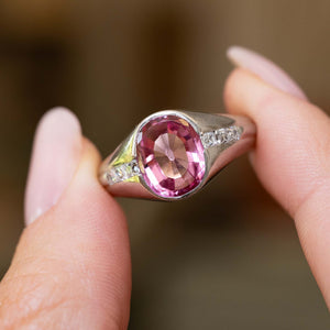 Fingers holding up a Vintage, 1940s pink sapphire and diamond gypsy ring against a blurred background