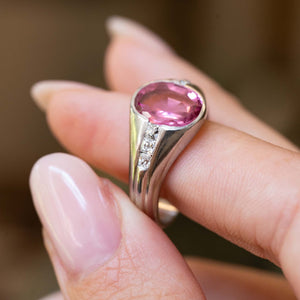 A finger holding a Vintage, 1940s pink sapphire and diamond gypsy ring in platinum against a blurred background.