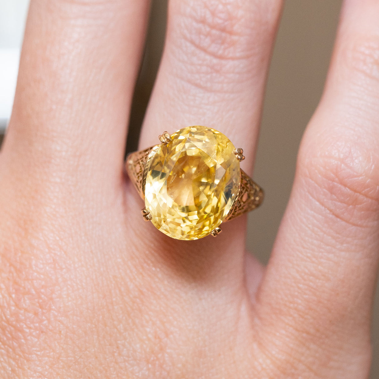 A close-up of a hand wearing a vintage, 1950s 19ct sunshine-yellow sapphire cocktail ring in yellow gold.