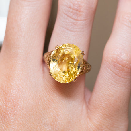 A close-up of a hand wearing a vintage, 1950s 19ct sunshine-yellow sapphire cocktail ring in yellow gold.