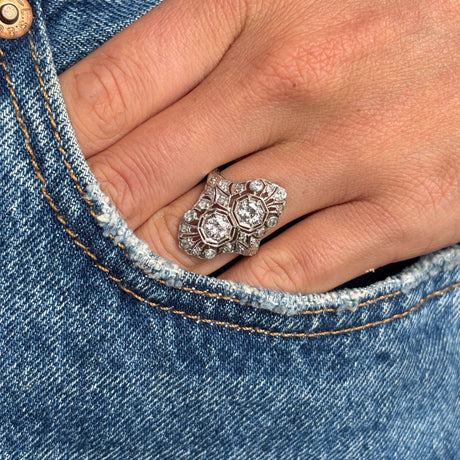 Antique Art Deco diamond cluster cocktail ring in platinum styled on hand against blue denim, showcasing the elaborate filigree setting and brilliant old-cut diamonds.