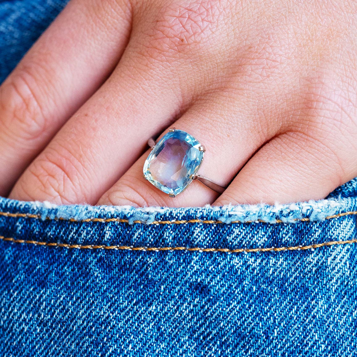 Blue sapphire solitaire ring worn on hand with denim pocket detail.