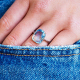 Blue sapphire solitaire ring worn on hand with denim pocket detail.