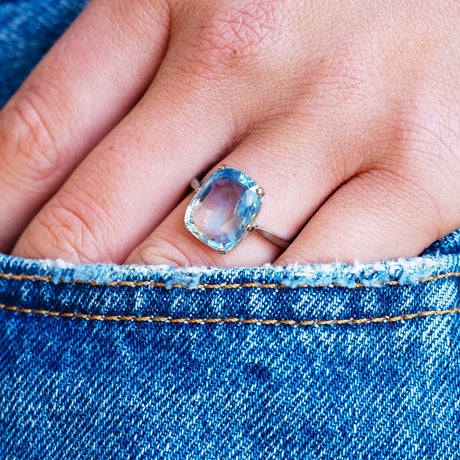 Blue sapphire solitaire ring worn on hand with denim pocket detail.