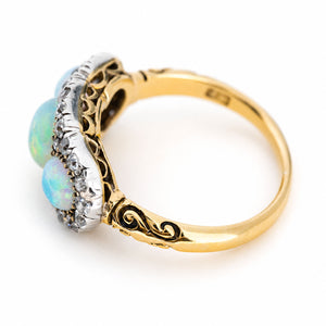 An antique three-stone round opal & diamond halo cluster ring with a yellow gold band and hand-engraved details in the band.