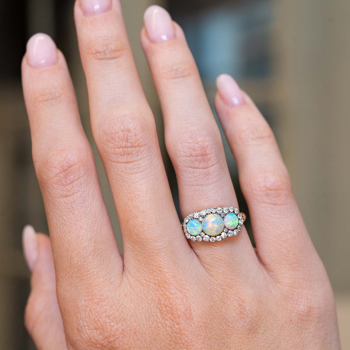An antique, Victorian three-stone opal & diamond cluster ring shown on a wider view of the hand.