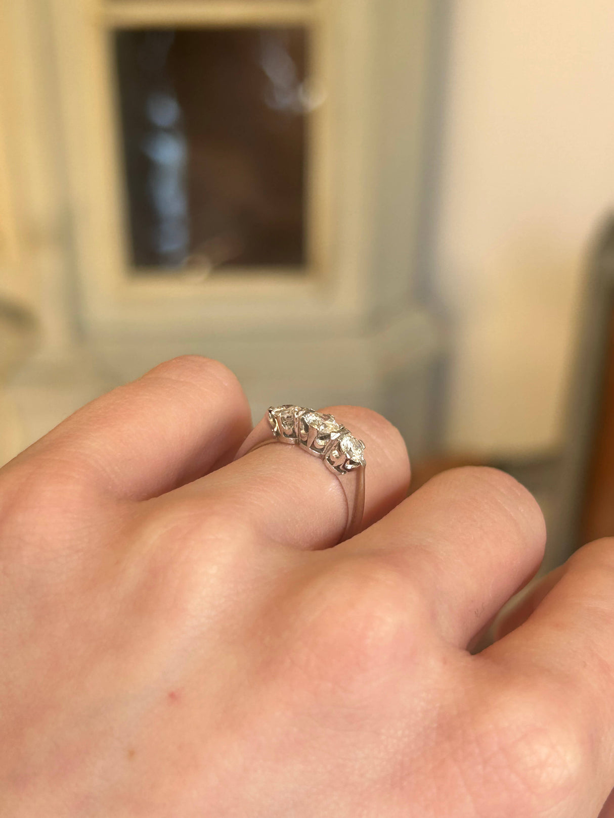Intricate side profile of 1950s white gold diamond three stone ring worn on hand.
