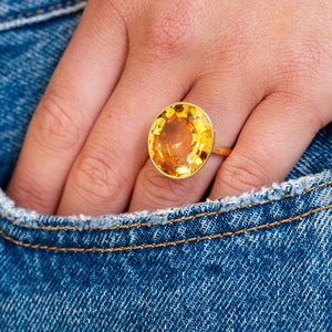 Hand wearing a gold ring with a orange topaz against a denim background.