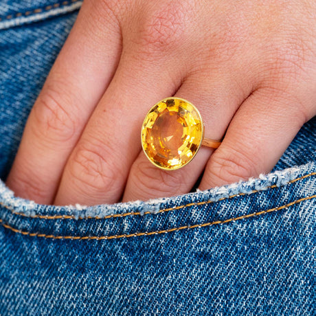 Hand wearing a gold ring with a orange topaz against a denim background.