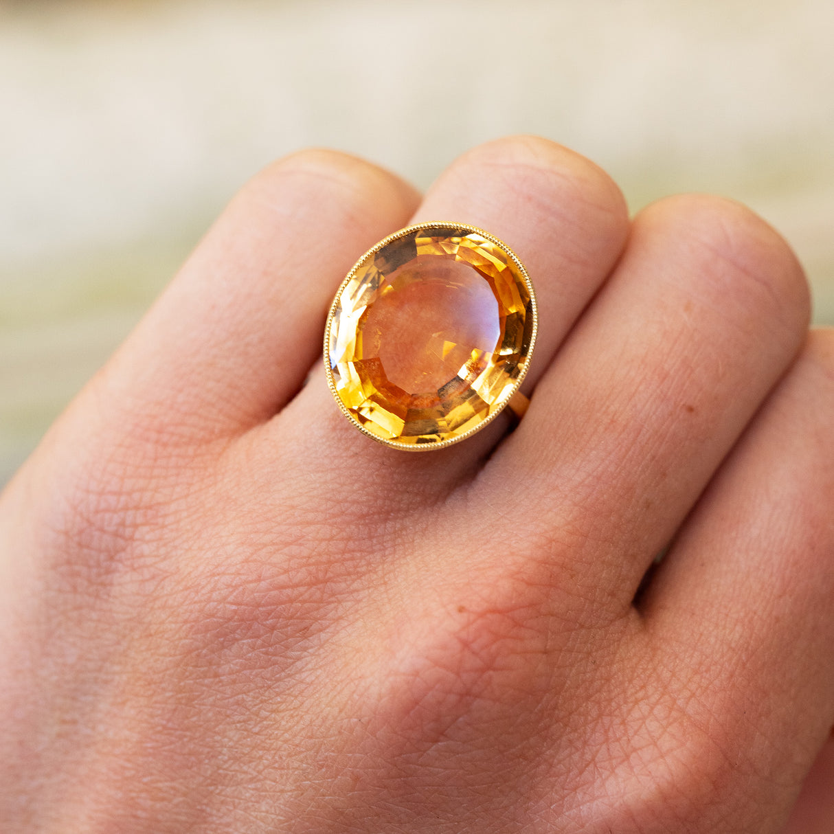 Gold ring with a large orange topaz on a hand against a blurred background.