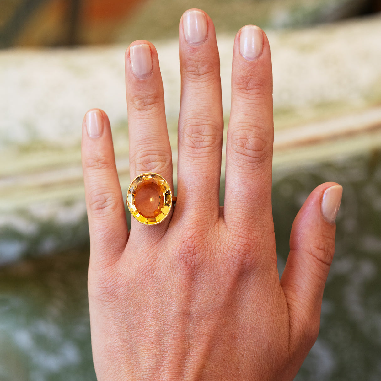 Orange topaz cocktail ring worn on hand with natural nails.