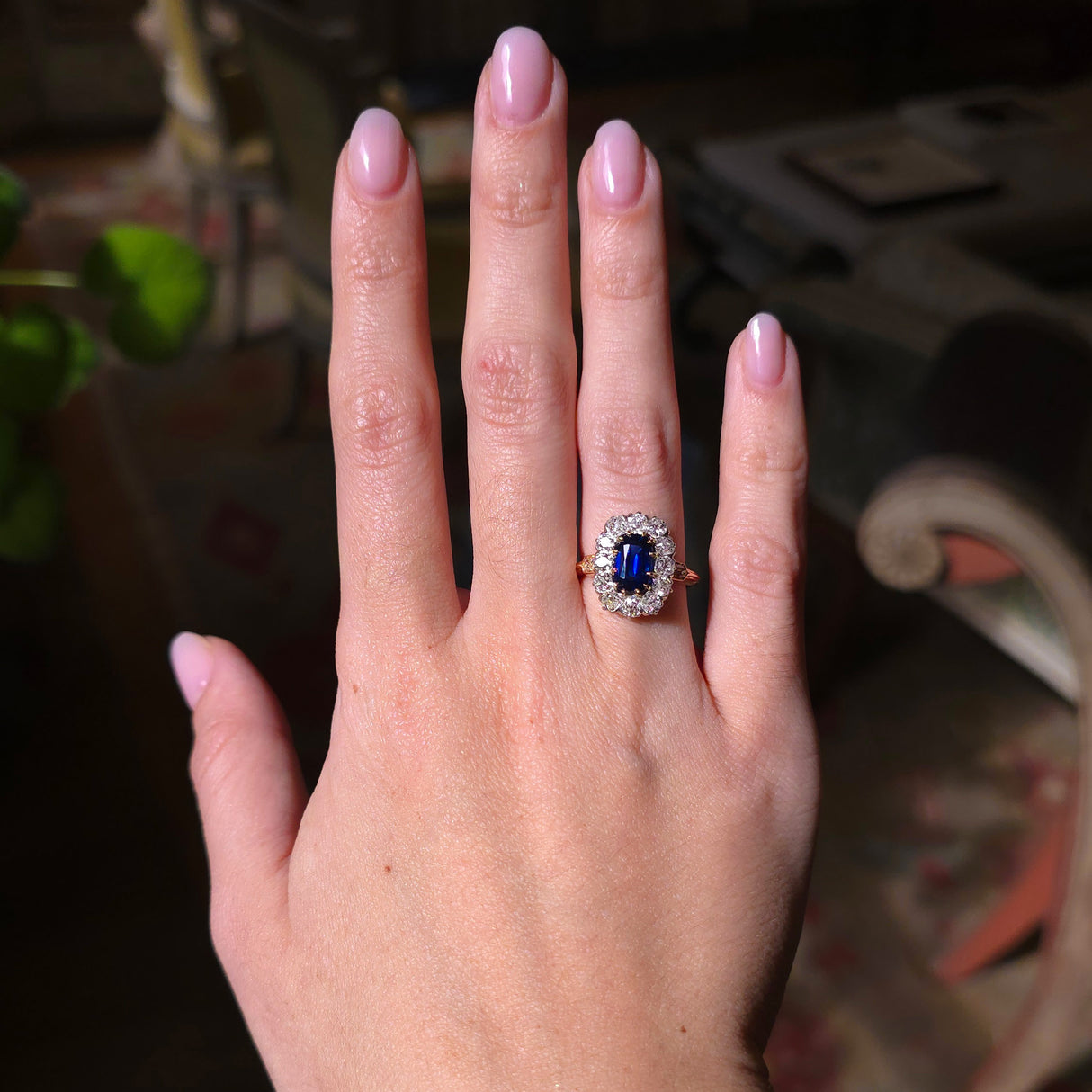 Blue sapphire and diamond cluster ring worn on the hand held out to show the ring in light