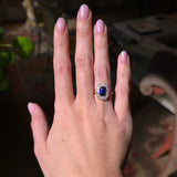 Blue sapphire and diamond cluster ring worn on the hand held out to show the ring in light
