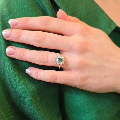 Emerald and diamond cluster ring worn on hand held against a green jacket