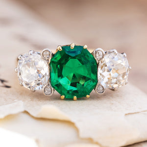 An antique Edwardian octagon-cut emerald and old-mine diamond three-stone engagement ring in yellow gold.
