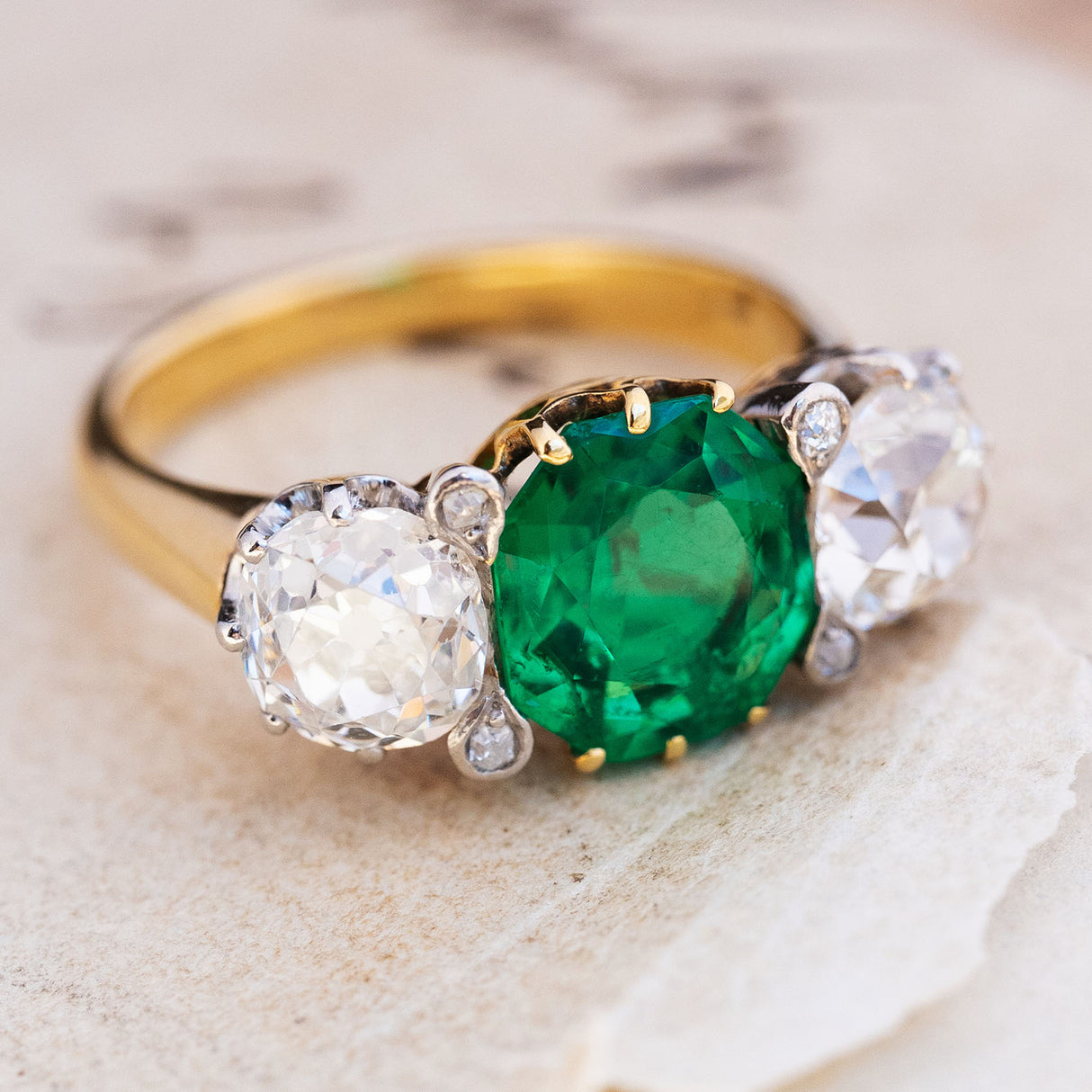 Three-quarter view of an antique Edwardian octagon-cut emerald and old-mine diamond three-stone engagement ring in yellow gold.