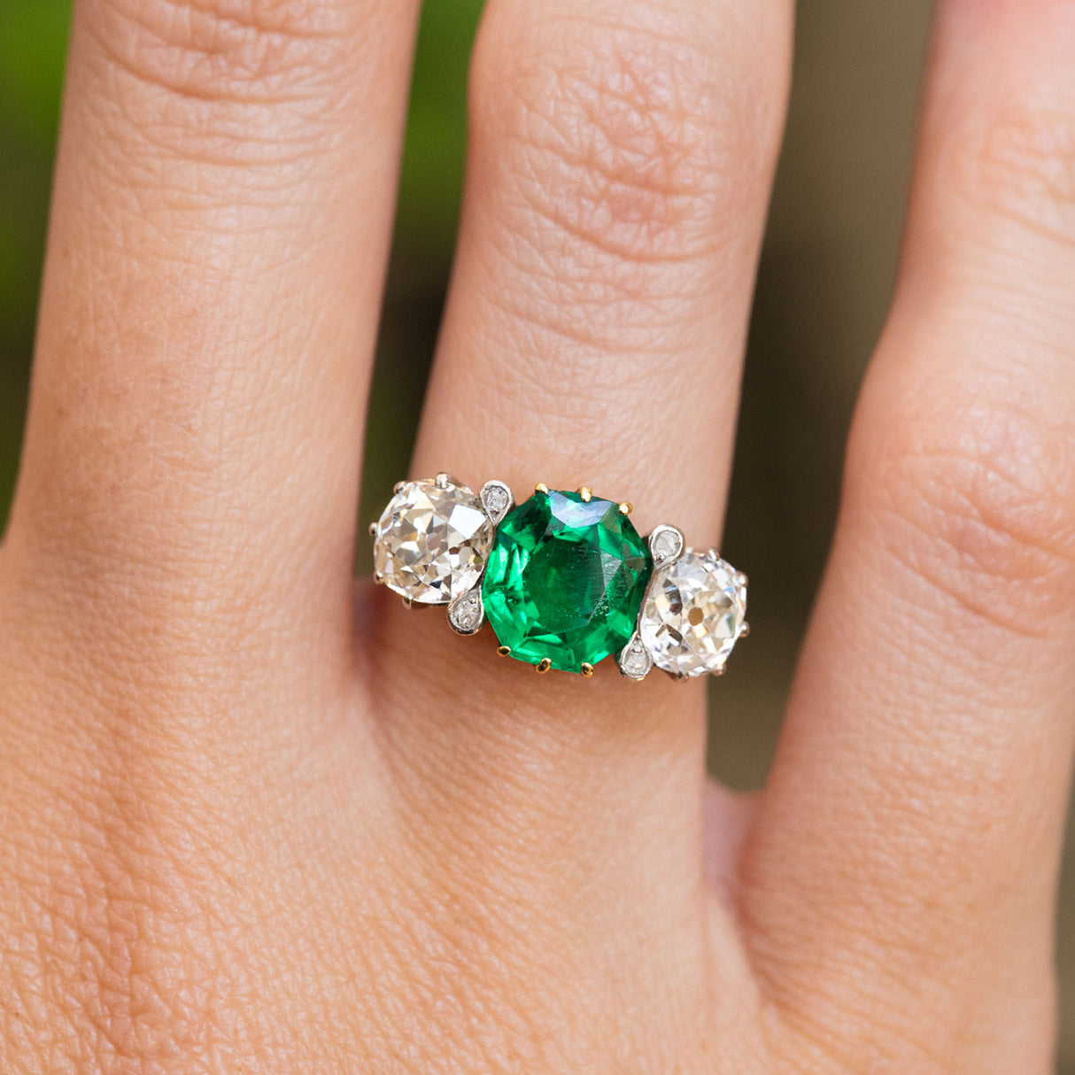 An antique Edwardian octagon-cut emerald and old-mine diamond three-stone engagement ring worn on the hand.