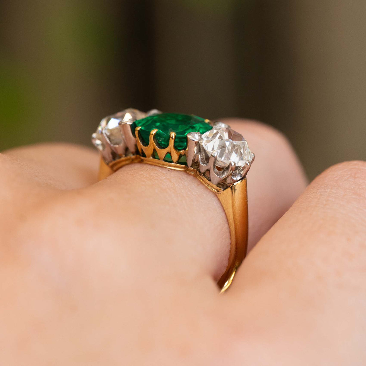 Side view of an antique Edwardian octagon-cut emerald and old-mine diamond three-stone engagement ring in yellow gold.