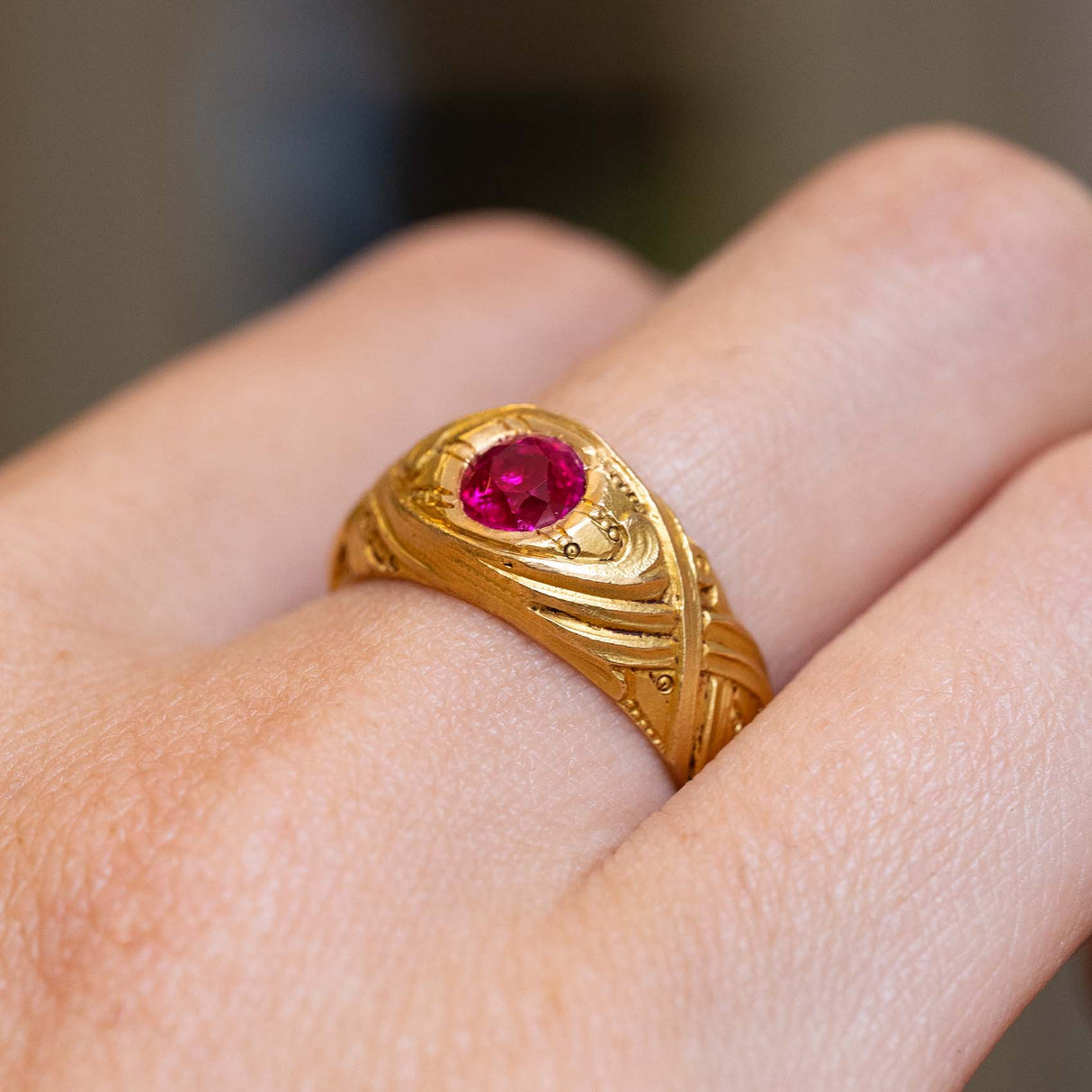 A hand up close wearing an Antique, Art Nouveau ruby single-stone yellow gold ring to show the profile of the ring