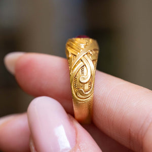 A close-up of a hand holding an Antique, yellow gold Art Nouveau ruby single-stone ring held in the fingers to show the shoulders of the ring.