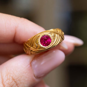 An Art Nouveau antique round ruby single-stone solitaire ring on a finger up close in yellow gold