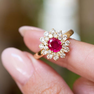 A vintage 1980s Burmese ruby and diamond cluster ring held between the fingers.